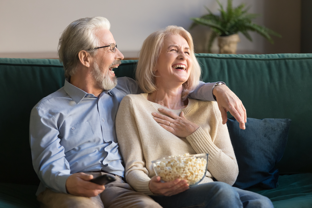 A senior couple laughs as they watch a movie